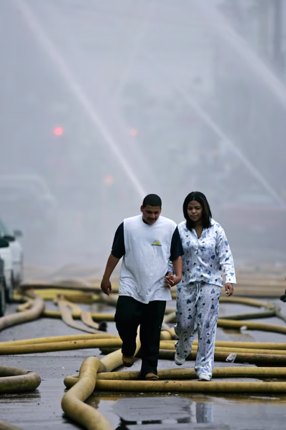 Two people&nbsp;who declined to give their names and were displaced from their home by the warehouse fire step over fire hoses early Wednesday in Philadelphia.