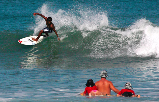 Foreign tourists watch a local surfer at a beach in Kuta