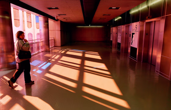 A woman walks through a Terminal A parking garage access corridor bathed in streams of red and yellow light at Logan International Airport in Boston. The colored light was generated by tinted window panes created by Christopher Janney as part of his interactive public art project at the airport.
