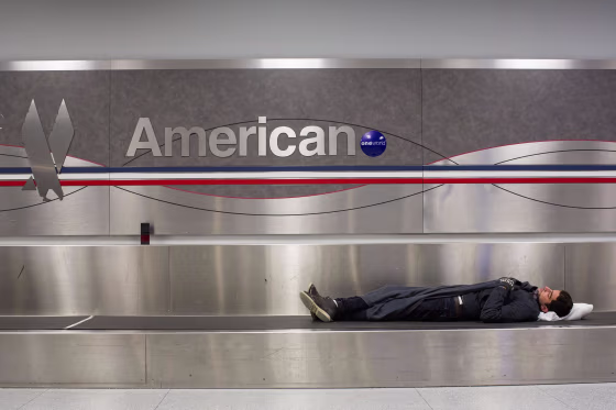 Image: A man sleeps on a conveyer belt under an American Airlines logo at John F. Kennedy International Airport in New York