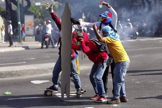 Image: Anti-government protesters take cover from the police behind makeshift shields in Caracas