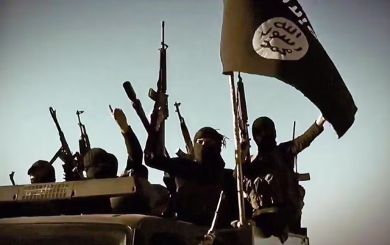 Image: ISIS fighters raise their weapons as they stand on a vehicle mounted with the group's flag