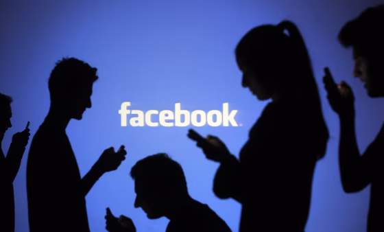 Image: People pose with mobile devices in front of projection of Facebook logo in this picture illustration taken in Zenica