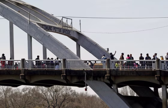 Image: People walk along the Edmund Pettus Bridge before the beginning of the 50th anniversary of the Selma to Montgomery civil rights march in Selma