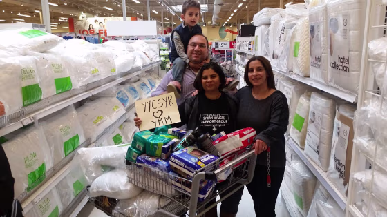 Saima Jamal, right, stands with Syrian newcomers Naser Nader and Rita Khallas as they shop for Fort McMurray evacuees. The sign they're holding up means "Syrians in Calgary love Fort McMurray."