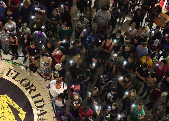 Image: People hold up their cellphones instead of candles as names of those killed are read aloud