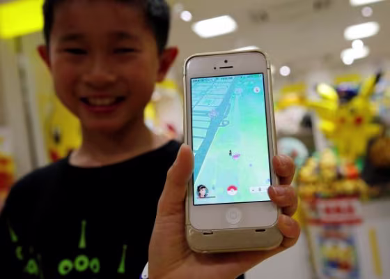 Boy poses with a mobile phone displaying the augmented reality mobile game "Pokemon Go" by Nintendoa in front of a shop selling Pokemon goods in Tokyo