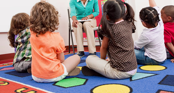 Teacher and children sitting on floors with hands raised