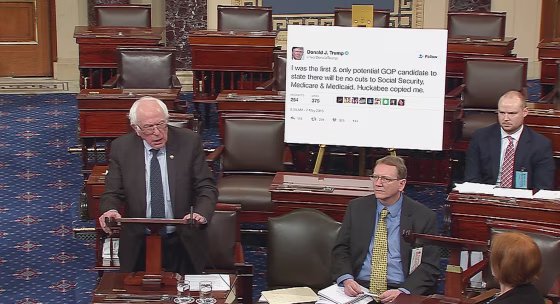 Image: Senator Bernie Sanders addresses the Senate floor while displaying a poster of a tweet by Donald Trump