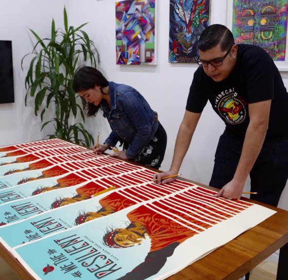 Artists Ernesto Yerena and Ayse Gursoz signing one of the posters in the "We the People" art series.