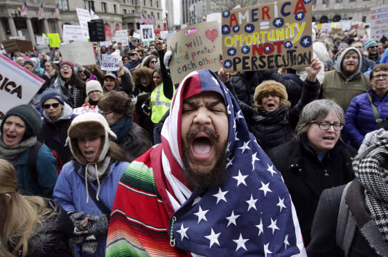 Image: Izzy Berdan, of Boston, center, wears an American flags as he chants slogans with other demonstrators during a rally