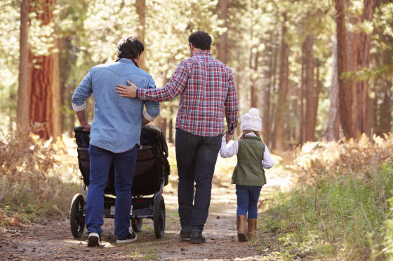 Gay Male Couple Pushing Children In Buggy Through Woods