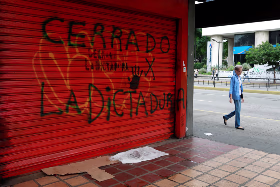 Image: A woman walks on a street close to a graffiti that reads \"closed because of the dictatorship\" during a national strike in Venezuela.