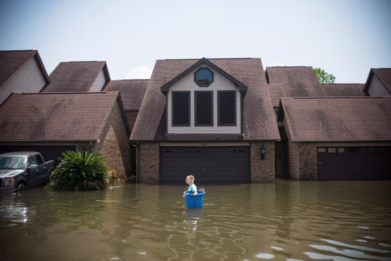 Image: Jenna Fountain carries a bucket down Regency Drive to try to recover items from their flooded home