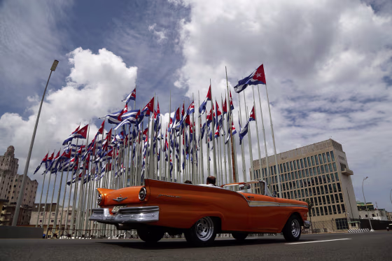 Image: Tourists ride a classic American convertible car along the Malecon beside the United States embassy as Cuban flags fly
