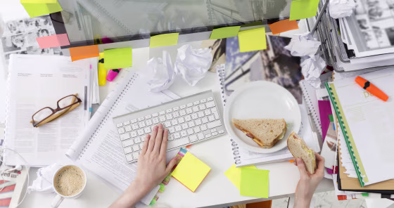Office wotker at messy office desk eating a sandwich