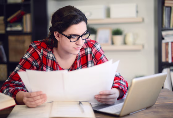 Image: A woman looks over papers over a laptop