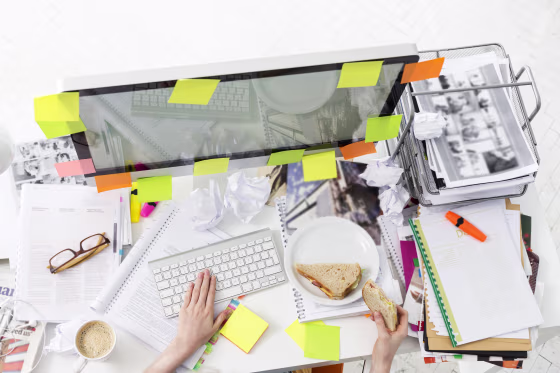 Image: Office wotker at messy office desk eating a sandwich