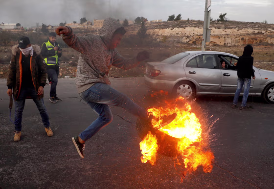 Image: A Palestinian kicks a burning tire during clashes with Israeli troops at a protest against U.S. President Donald Trump's decision to recognize Jerusalem as Israel's capital, near the Jewish settlement of Beit El, near the West Bank city of Ramallah