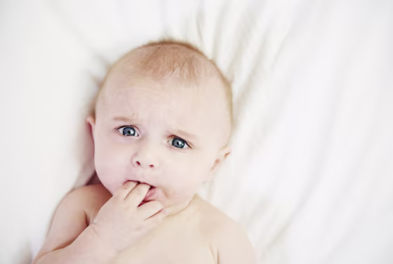 Baby in bed with fingers in mouth