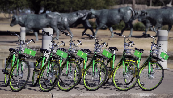 Image: Shared bikes are lined up on a sidewalk by a popular tourist destination in Dallas