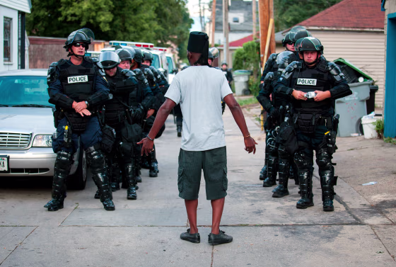 Image: A man talks to police in riot gear as they wait in an alley after a second night of clashes between protesters and police