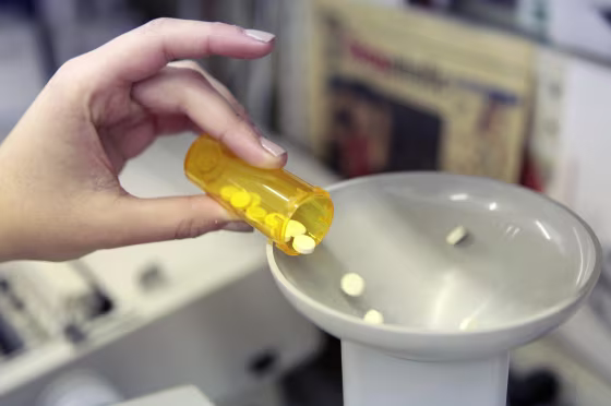 Image: A pharmacy employee dumps pills into a pill counting machine as she fills a prescription.