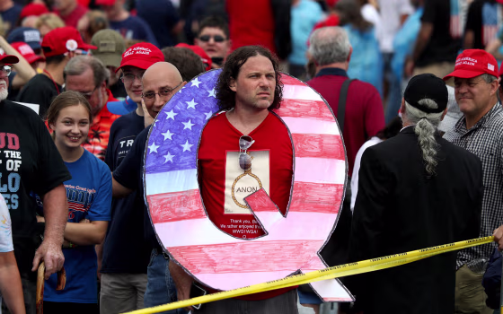 Image: David Reinert holds a large \"Q\" sign while waiting to see Trump