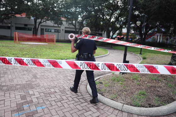 Image: An officer uses police tape to keep people out as law enforcement investigates a shooting at the Jacksonville Landing