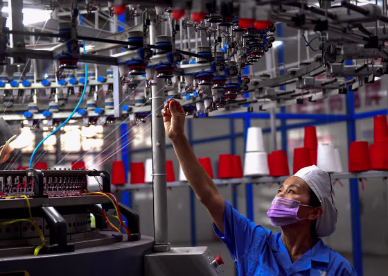 Image: An employee monitors a circular weaving machine at a textile factory in Shangqiu, China