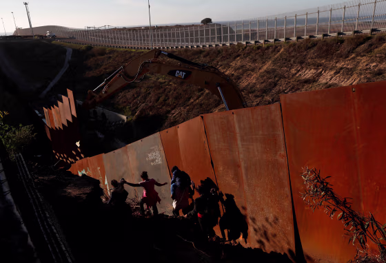 Image: Migrants climb down a steep hill after giving up on trying to climb the border wall into the U.S. from Tijuana