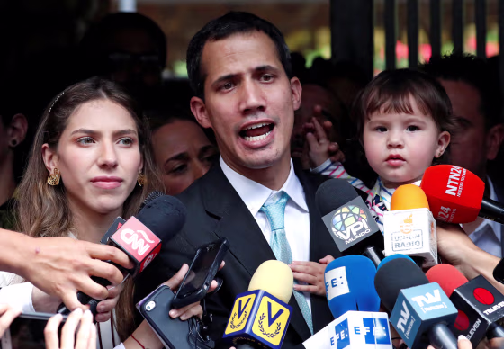 Image: Venezuelan opposition leader and self-proclaimed interim president Juan Guaido talks to media next to his wife Fabiana Rosales, while carrying their daughter outside their home in Caracas