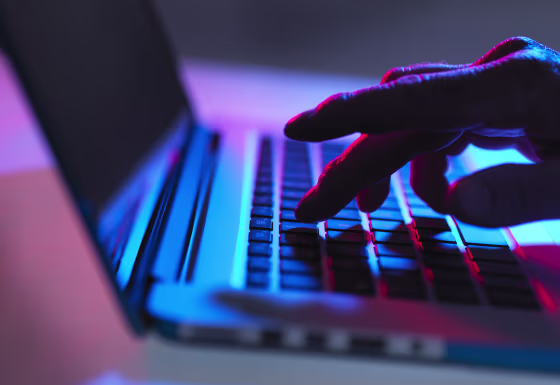 Silhouette of male hand typing on laptop keyboard at night