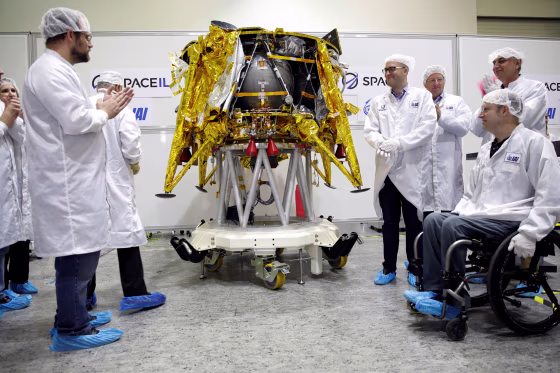Members of Israeli non-profit group SpaceIL and representatives from Israel Aerospace Industries (IAI) stand next to an unmanned spacecraft during a presentation to the media in Yehud, Israel