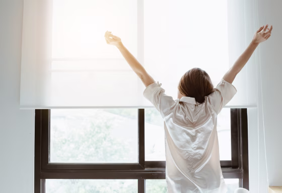 Image: Portrait of woman stretching near the window after her wake up in the morning, back view.