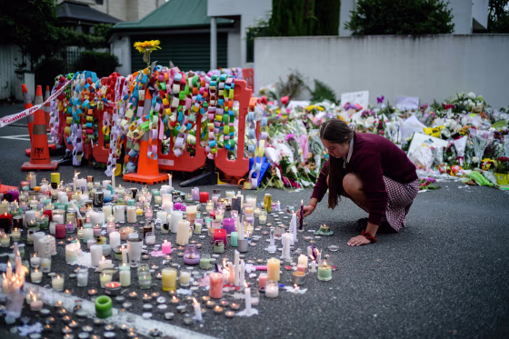 Image: A student places a candle next to flower tributes for the victims after a vigil in Christchurch