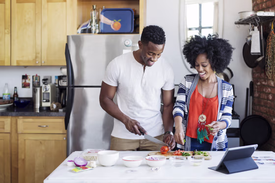 Happy man cutting tomatoes while standing with girlfriend at home
