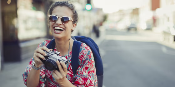 Portrait laughing, enthusiastic young female tourist in sunglasses photographing with camera on urban street