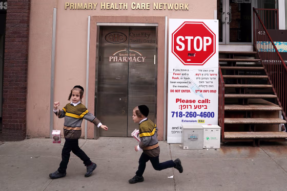 Image: Children walk past a sign advising about a measles outbreak in the Brooklyn Borough of New York