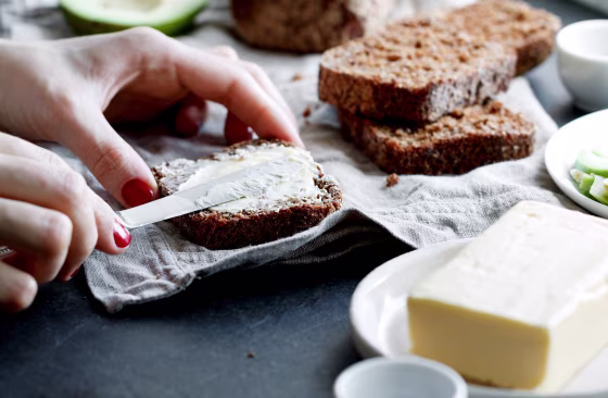 Close-Up Of Woman Applying Butter On Bread In Plate On Table