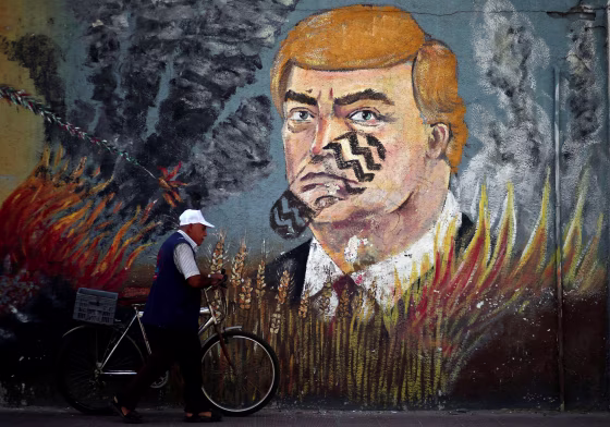 Image: Palestinian man walks with his bicycle past a mural depicting U.S. President Donald Trump, in Gaza City