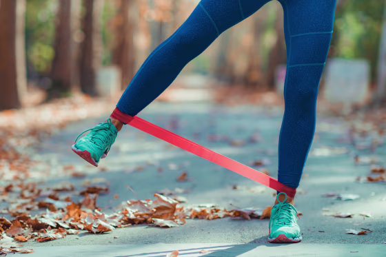 Image: Low Section Of Woman Exercising With Resistance Band On Road During Autumn