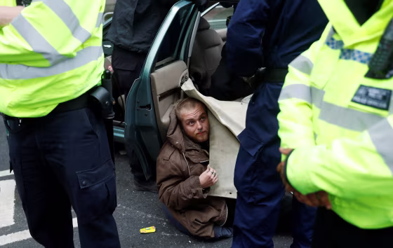 Image: Police officers remove a protester attached to a car during Extinction Rebellion protesters demonstrate in Westminster, London