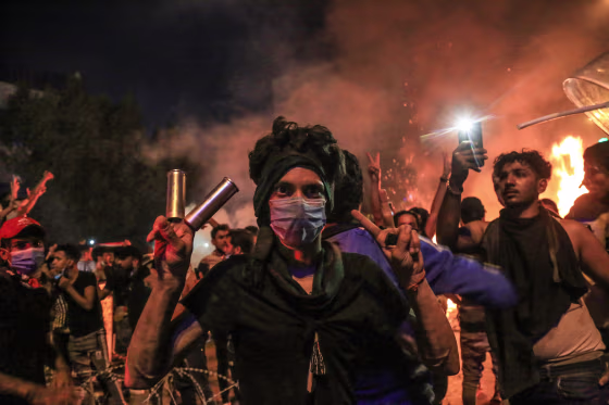 Image: A protester wears tear gas canisters on his fingers and gestures the victory sign during anti-government protests in the Shiite shrine city of Karbala, south of Iraq's capital Baghdad