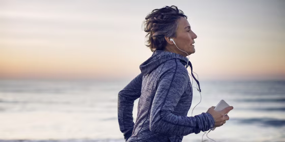 Woman jogging while listening music at beach against sky