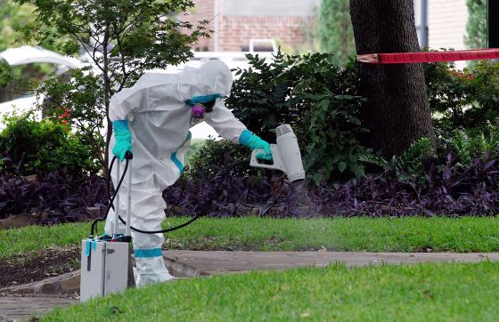 Image: A man dressed in protective hazmat clothing treats the sidewalk in front of an apartment where nurse Nina Pham resides