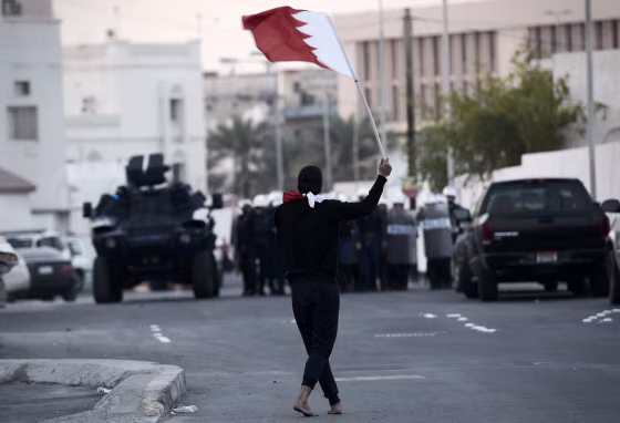 A protester holds a Bahraini flag in front of riot police during clashes after a protest against the arrest of the head of the banned Shiite opposition movement, Sheikh Ali Salman, on Dec. 29, 2014, in Manama. 