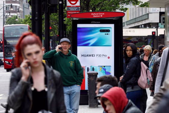 Image: Pedestrians use their mobile phones near a Huawei advert at a bus stop in central London
