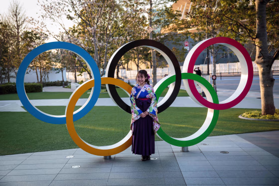 Image: A woman wearing a traditional Japanese kimono poses next to the Olympic rings in front of the Japan National Stadium, the main venue for the Tokyo 2020 Olympic Games, in Tokyo.