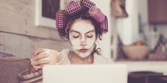 Woman With Hair Curlers Using Laptop On Sofa At Home
